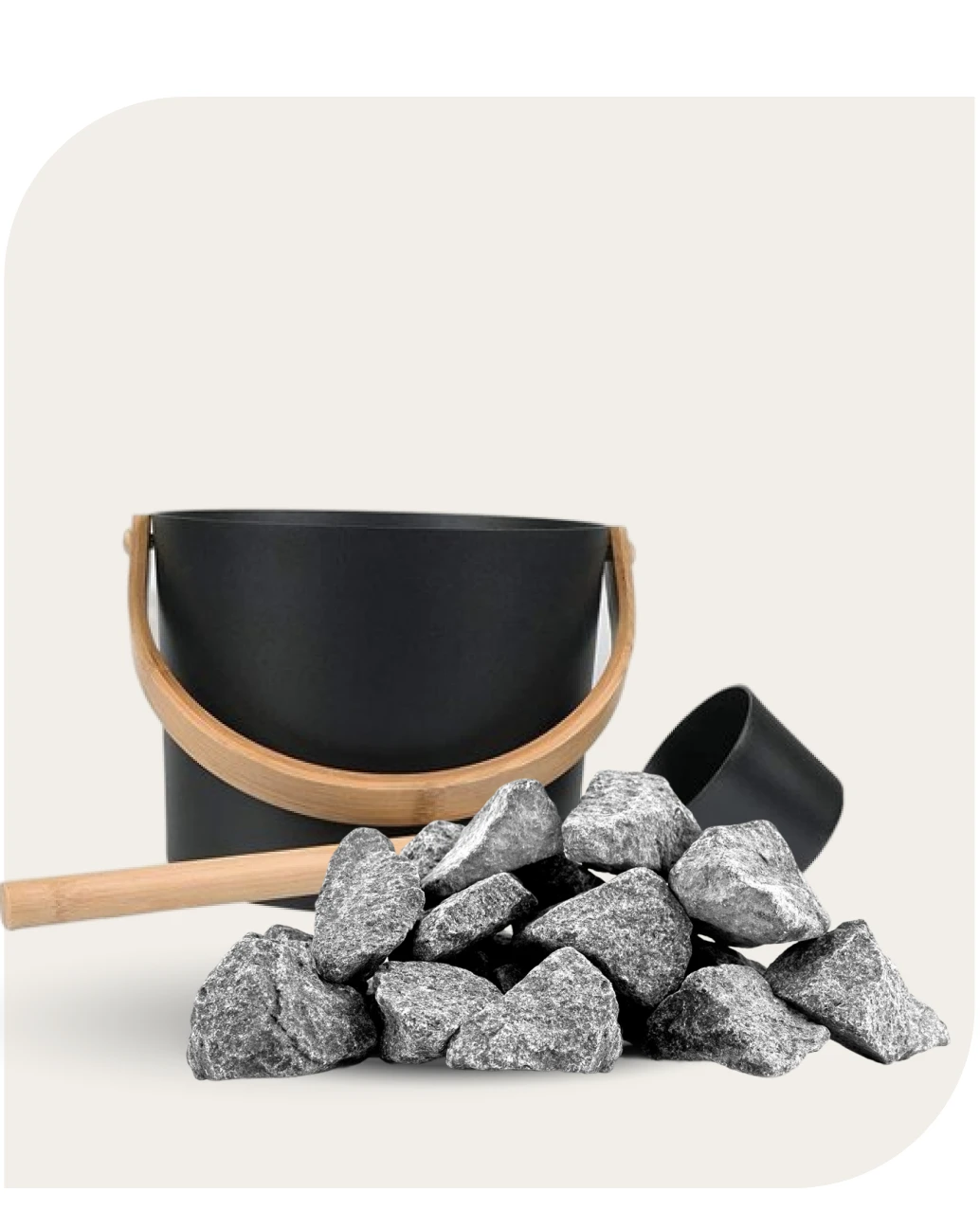 Black sauna bucket and ladle with wooden handles beside grey sauna stones on a cream background