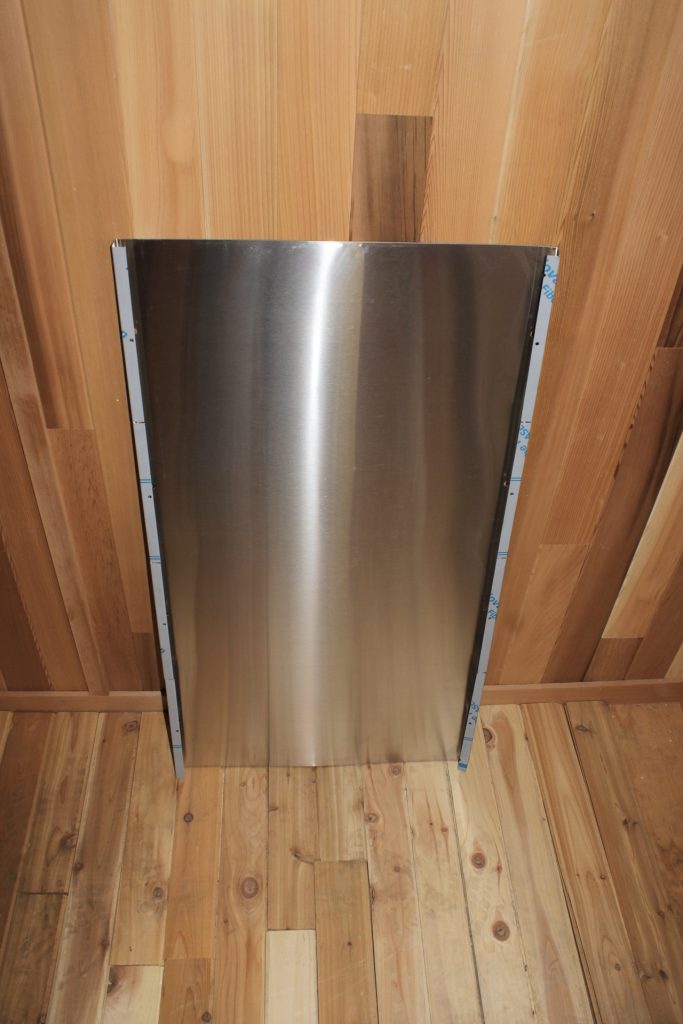 Stainless steel heat shield mounted flat against a cedar sauna ceiling