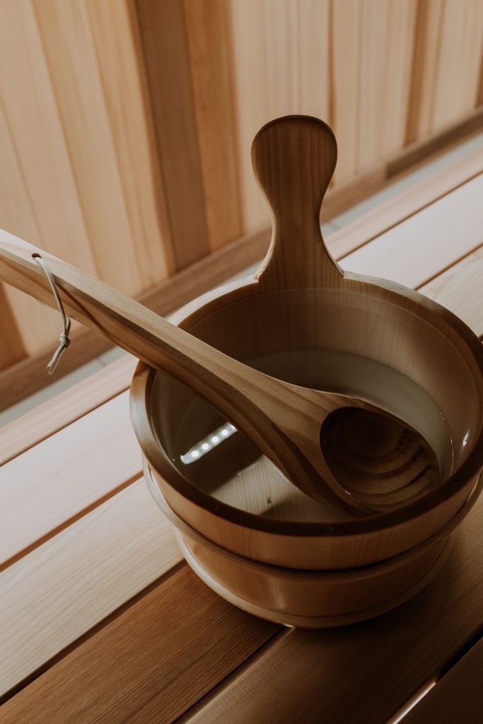 Wooden sauna bucket with a long ladle across its rim on a warm cedar bench