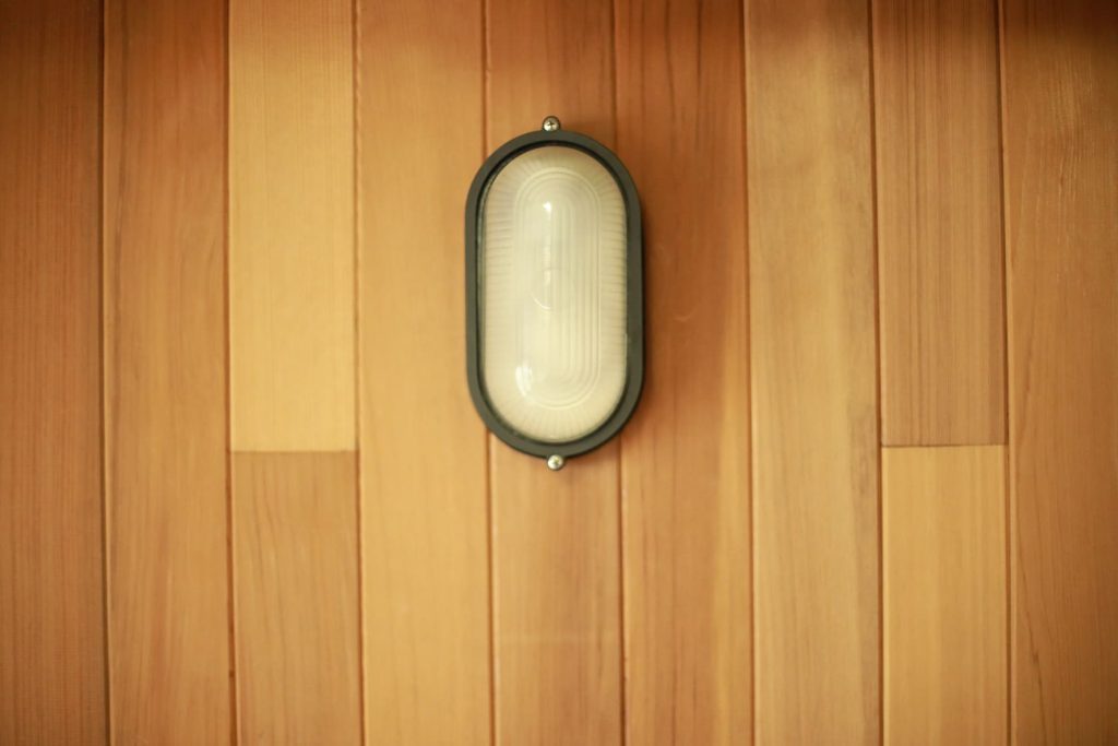 Oval sauna light with a frosted cover and dark protective cage mounted on a cedar wall