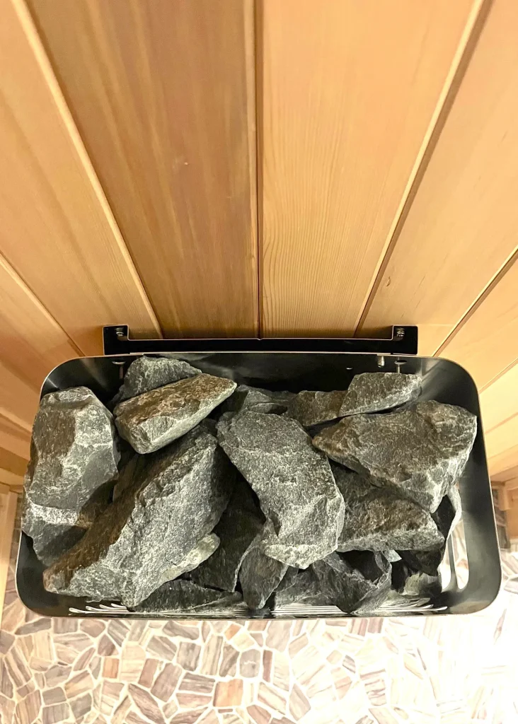 Black sauna ceiling heat shield filled with dark stones below a pale cedar ceiling