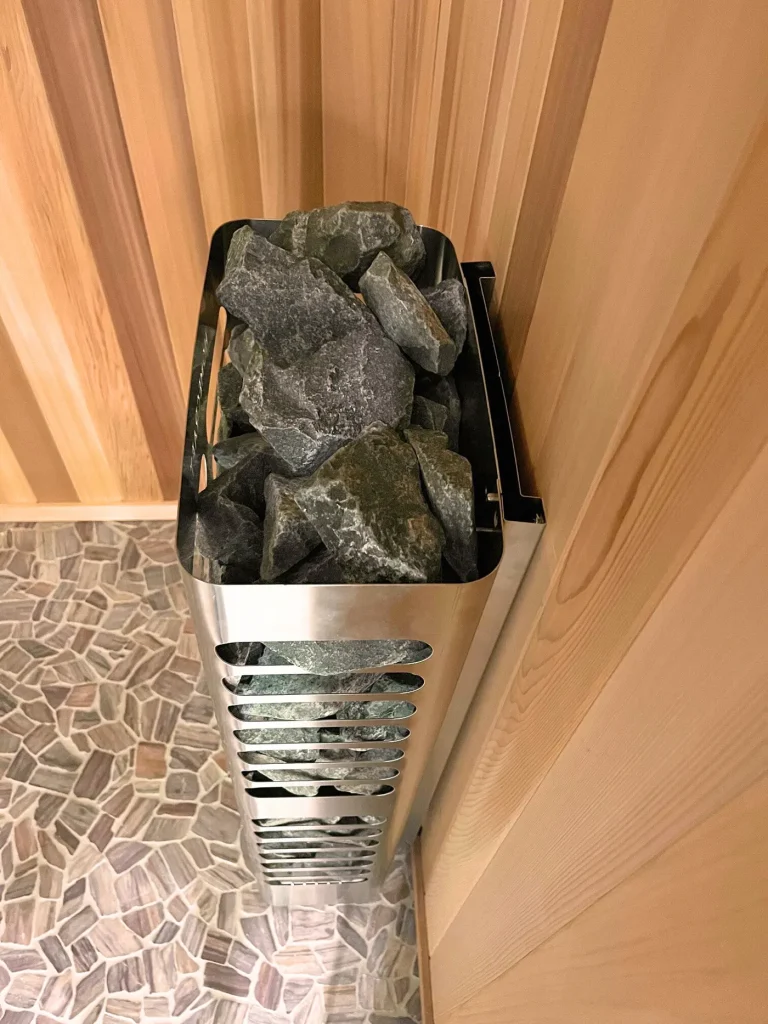 Slim sauna heater with a stainless heat shield in a cedar corner above mosaic tile