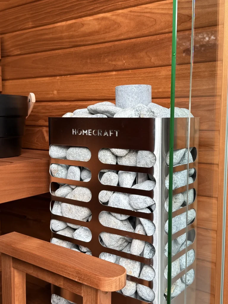 Pale soapstone sauna rocks filling a Revive Slim heater beside cedar, glass and a bench