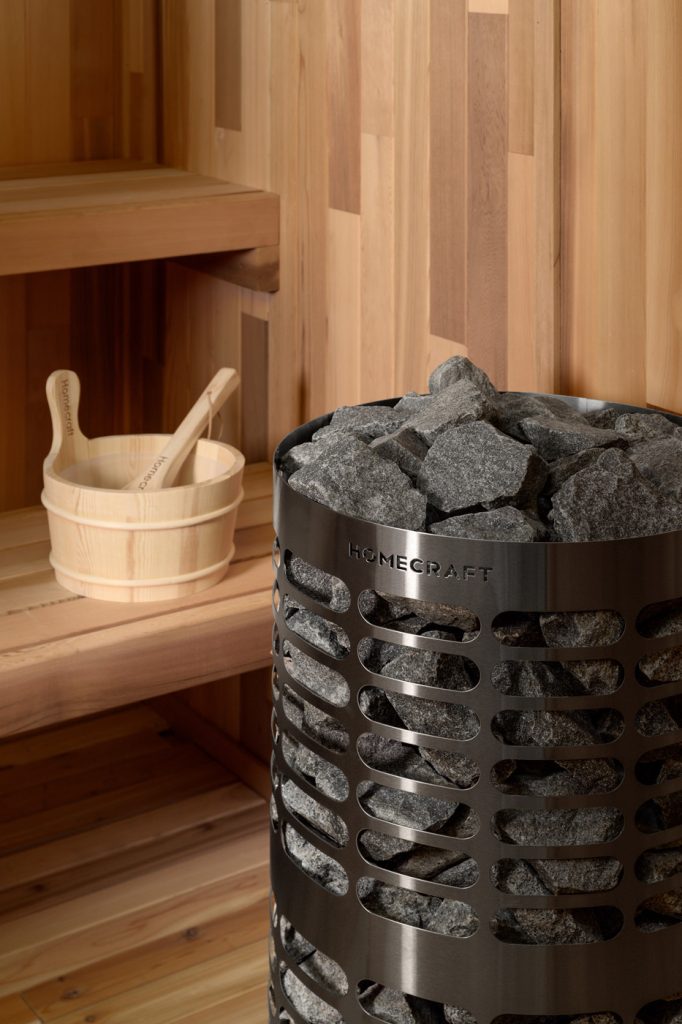 Homecraft Apex sauna heater in a cedar sauna, with a wooden bucket and ladle on the bench behind
