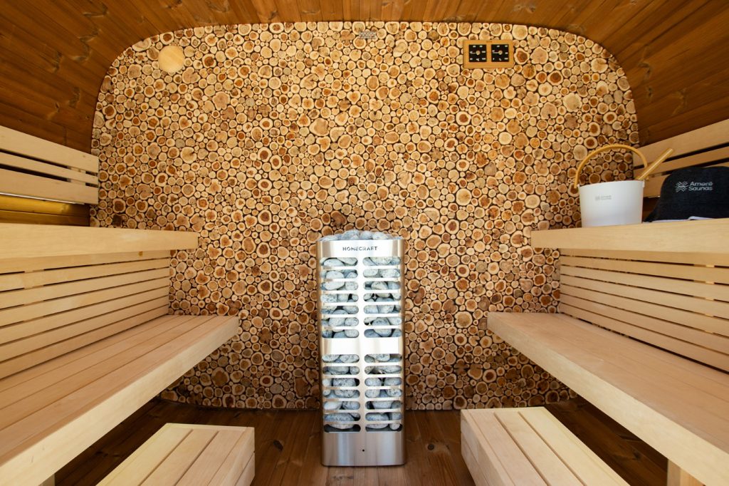 Custom sauna with wood round wall Custom Canadian sauna kit with pale benches, end-cut wood feature wall and cylindrical Homecraft heater