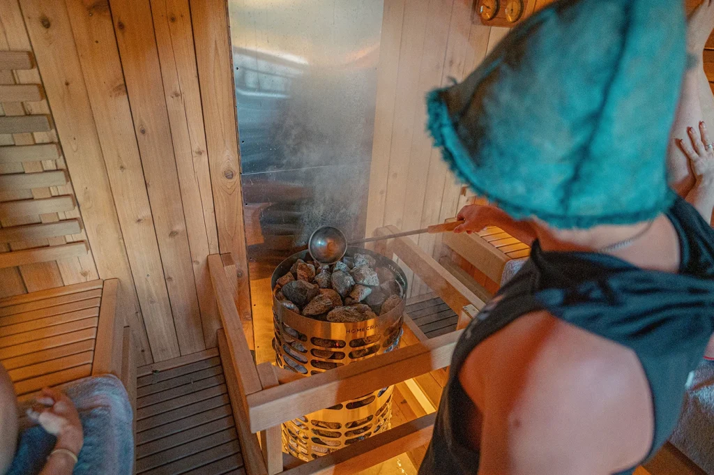 Water being poured onto the stones of a sauna heater in a cedar room