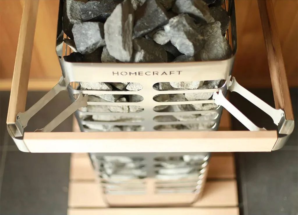 Homecraft Revive sauna heater guard with a pale wooden rail, steel bracket and grey stones below