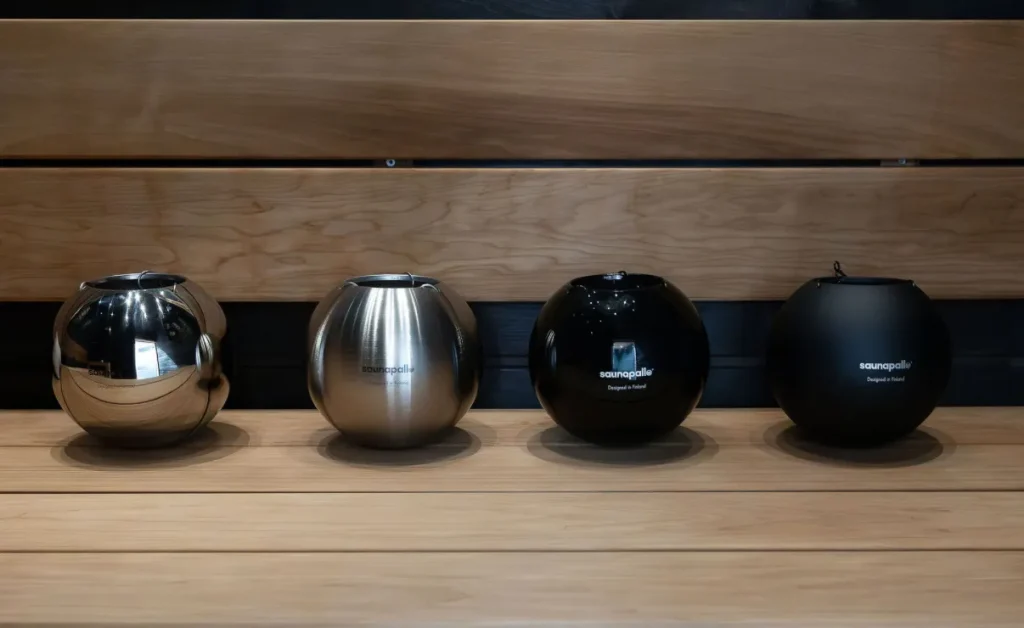 Four SaunaPallo sauna accessories in polished chrome, brushed steel, gloss black and matte black on cedar
