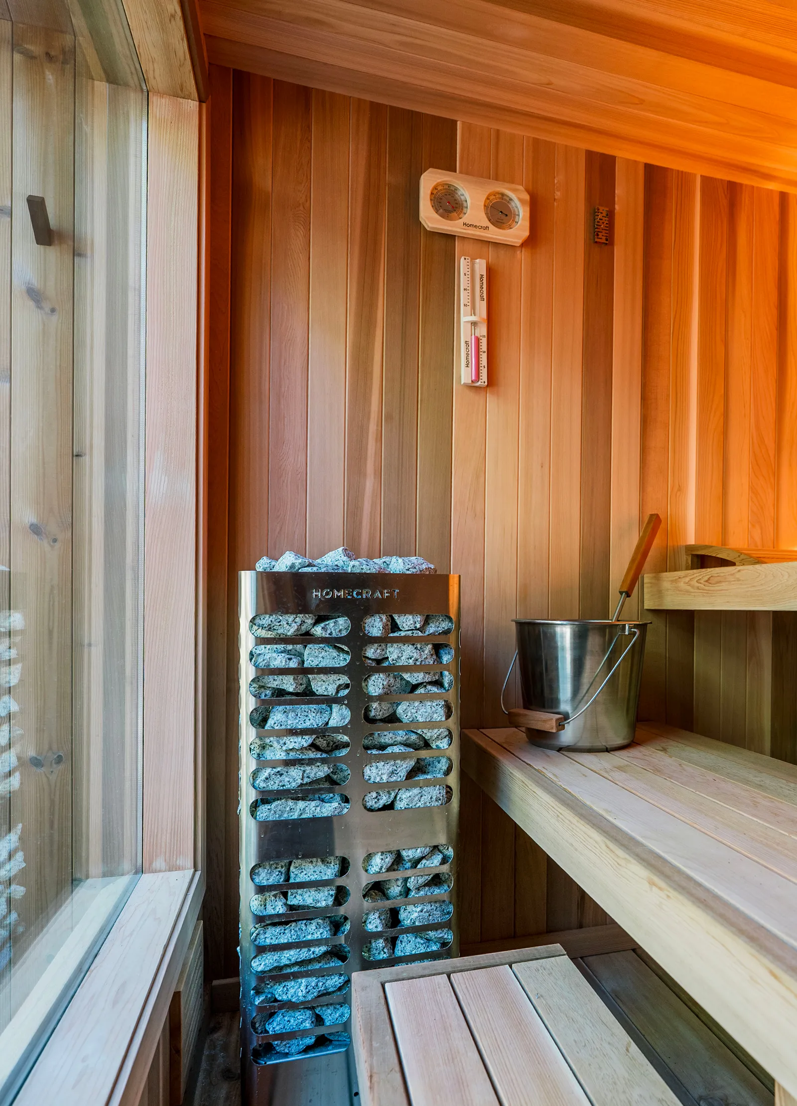 Cedar sauna interior with benches, a small window and a Homecraft heater glowing blue near the floor.