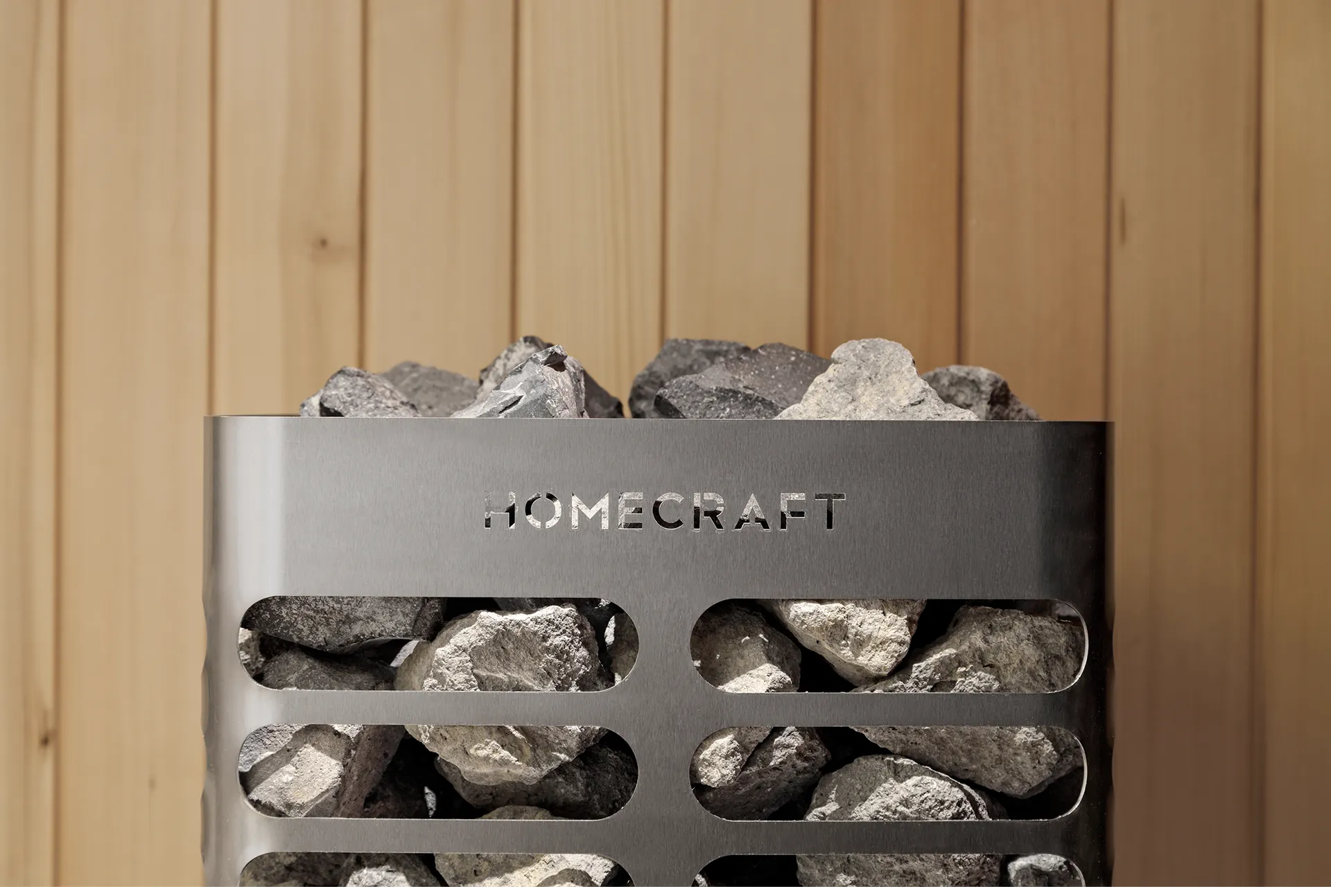 Rough stones packed into a Homecraft sauna heater above its vented steel body, with cedar boards behind
